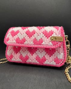 a pink and white cross body bag on a gold chain hanging from a black background