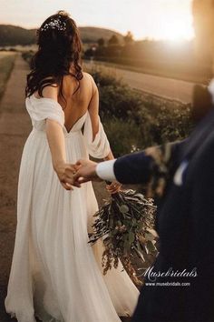 a bride and groom walking down the road holding hands