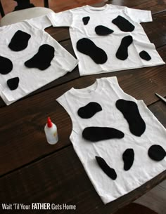 four t - shirts with black and white cow print on them sitting on top of a wooden table