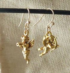 Our stunning Gold Cherub Cupid Angel drop earrings - the perfect accessory for any romantic occasion or as a special gift for someone dear to your heart. Crafted from solid 925 sterling silver and plated with 24K gold, these earrings boast a stunning vermeil finish. The earwires are made from gold-plated bronze. One earring features a beautiful cherub cupid angel blowing a horn and the other aiming a love arrow, symbolizing the power of love and passion. Our Gold Cherub Cupid Angel drop earrings Cupid Jewelry, Cupid Earrings, Angel Charms, Love Arrow, Angel Earrings, One Earring, Power Of Love, Earrings Christmas, The Power Of Love