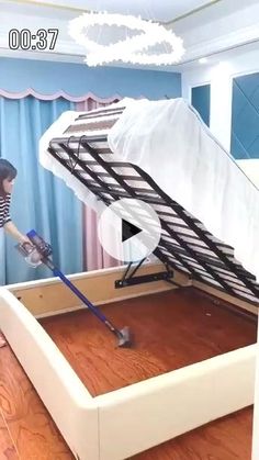 a woman is using a vacuum to clean the bottom of a bed with a mattress on it