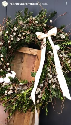 a wreath with white flowers and greenery tied to the front of a wooden box