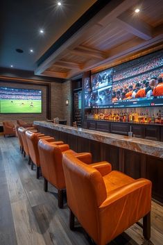 an empty bar with orange chairs and a large screen on the wall behind it in a sports stadium