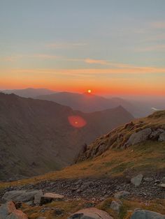 the sun is setting in the distance on top of a mountain with rocks and grass