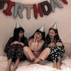 three women wearing party hats sitting on a bed with the words happy birthday hanging above them