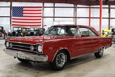 an old red car is parked in front of the american flag and other classic cars