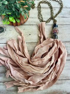 a scarf is laying on the ground next to a potted plant and a necklace