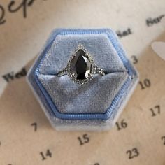 a black diamond ring sitting on top of a blue velvet covered box next to numbers