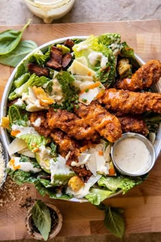 a salad with chicken wings and dressing in a white bowl on a wooden cutting board