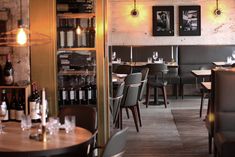 an empty restaurant with tables and chairs, bottles of wine on the wall behind them