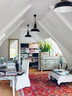 an attic bedroom is decorated in white and has a red rug on the floor, along with two lamps hanging from the ceiling