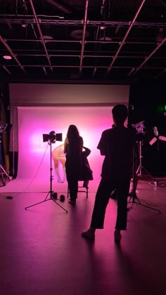 two people standing in front of a pink backdrop with lights behind them and camera equipment on the floor