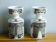 two black and white vases sitting on top of a wooden table next to each other