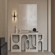 a white table with books on it in front of a wall mounted art piece and lamp