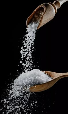 spoons filled with sugar and salt on top of each other in front of a black background