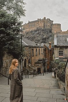 a woman is standing on the sidewalk in front of an old building with a castle behind her