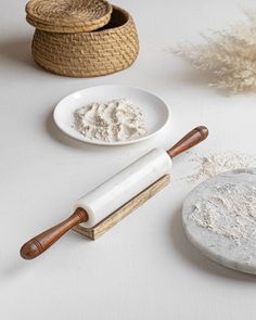 two bowls and a rolling pin on a white surface with some plants in the background