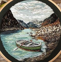 an embroidered picture of a boat on the water with mountains in the background and grass around it