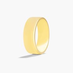 a plain yellow wedding ring on a white background with the light reflecting off of it's surface