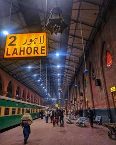 people are walking through the train station with signs hanging from the ceiling and lights above them