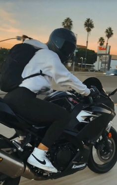 a man riding on the back of a motorcycle down a street with palm trees in the background