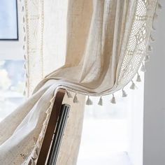 an open window with white curtains and tassels