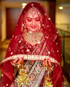 a woman in a red and gold bridal outfit holding a tray with jewelry on it