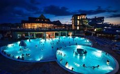 an outdoor swimming pool at night with people in the water and onlookers