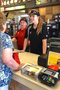 a woman standing at a counter in a fast food restaurant with two men behind her