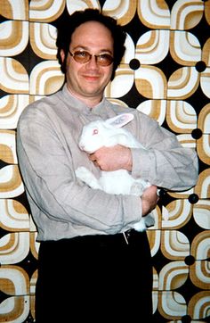 a man holding a rabbit in front of a wall with geometric designs on the walls