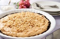 a pie sitting on top of a white plate covered in frosting and nuts next to flowers