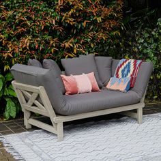 a gray couch with pillows on it sitting in front of some bushes and shrubbery