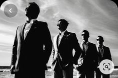 black and white photograph of four men in suits standing on the beach looking off into the distance