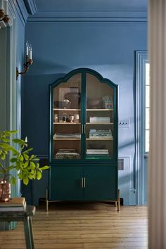 a room with blue walls and wooden flooring has a china cabinet in the corner