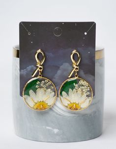 a pair of white and yellow flower earrings sitting on top of a marble stand next to a cup