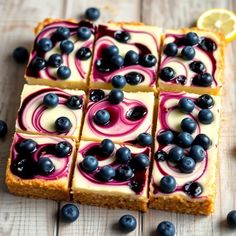 blueberry cheesecake squares are arranged on a wooden table with lemon slices and blueberries