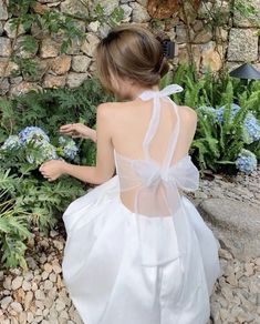 a woman in a white dress sitting on the ground next to some plants and flowers