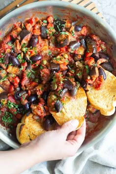 someone is holding up some bread with black olives and tomato sauce on it in a skillet