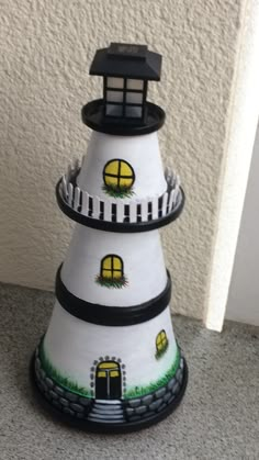 a white and black tower with a light house on it's top, sitting in front of a wall