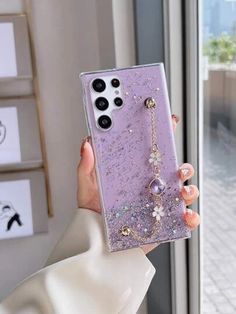 a person holding up a purple phone case with flowers and pearls on the front, in front of a window