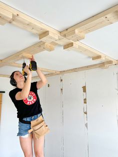 a woman in black shirt and blue shorts working on wooden beams with drill hammers