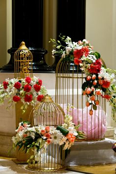 three bird cages with flowers in them sitting on the floor next to each other,