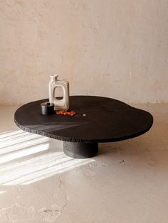 a black table with a white vase sitting on it's top and light coming through the window