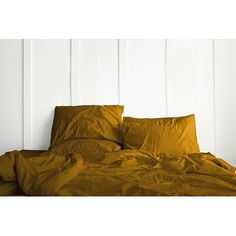 an unmade bed with yellow sheets and pillows on top of it, against a white wall