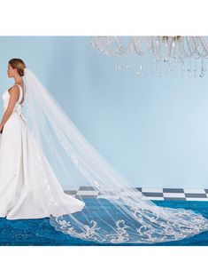 a woman in a wedding dress and veil standing on a blue carpet with a chandelier