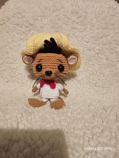 a small crocheted rat with a hat on it's head sitting on a white blanket