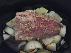 the meat is being cooked in the slow cooker with onions and garlic around it