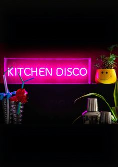 there is a neon sign that says kitchen disco next to some potted plants in front of it