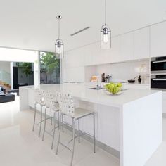 a white kitchen with lots of counter space and chairs around the island, in front of an open living area