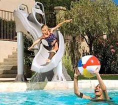 two people are playing in the pool with a beach ball and water slide behind them